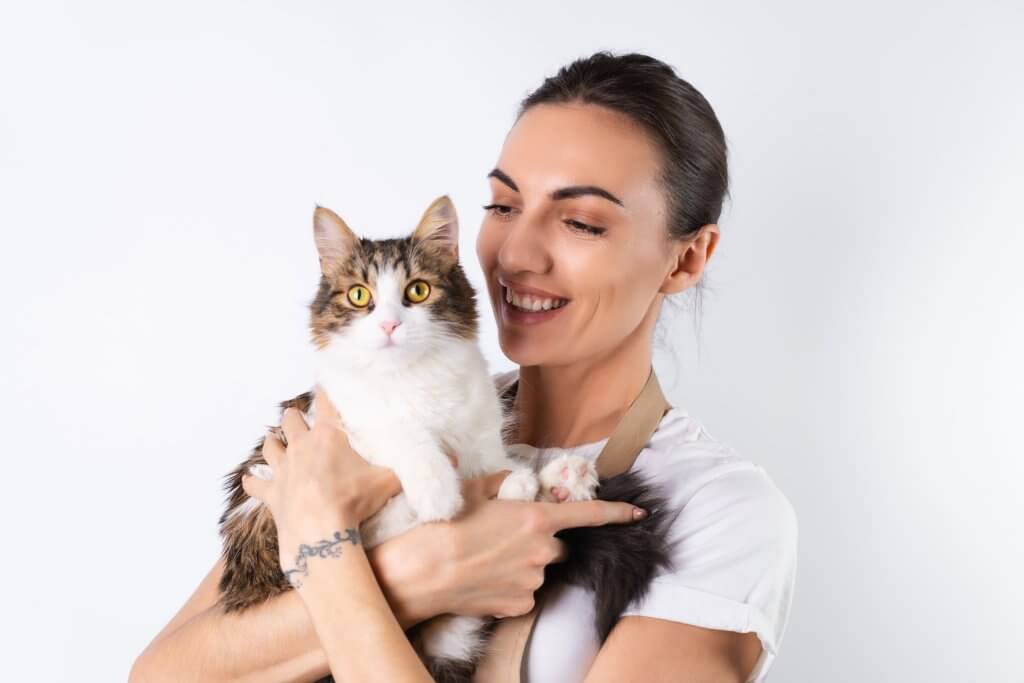 Mulher sorrindo e abraçando seu gato de pelagem longa marrom e branca, mostrando o vínculo afetivo e como entender por que os gatos derrubam coisas.